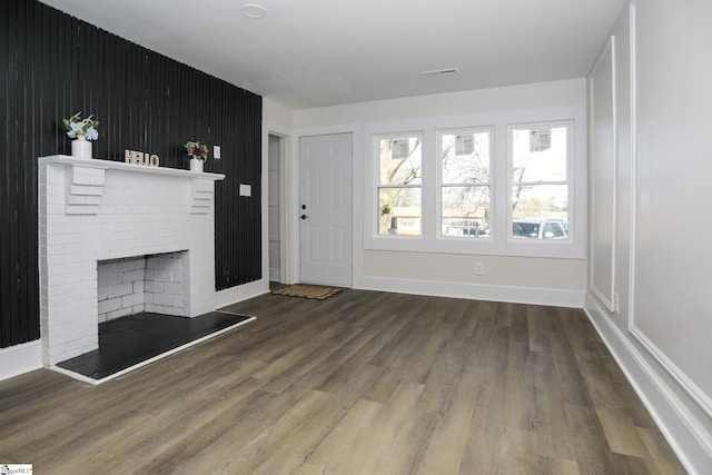 unfurnished living room with visible vents, baseboards, a brick fireplace, and wood finished floors