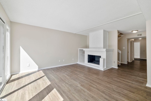 unfurnished living room with visible vents, a brick fireplace, baseboards, stairs, and wood finished floors