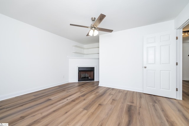 unfurnished living room featuring ceiling fan, a fireplace, baseboards, and wood finished floors