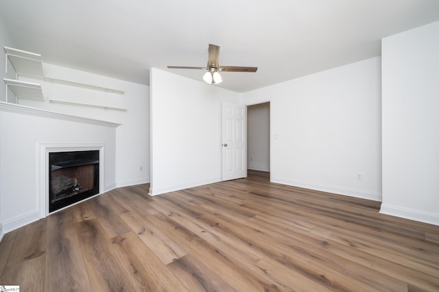 unfurnished living room with wood finished floors, a fireplace, baseboards, and ceiling fan