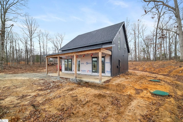 back of property with roof with shingles and a patio area