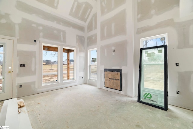 unfurnished living room with a wealth of natural light, heating unit, and a high ceiling