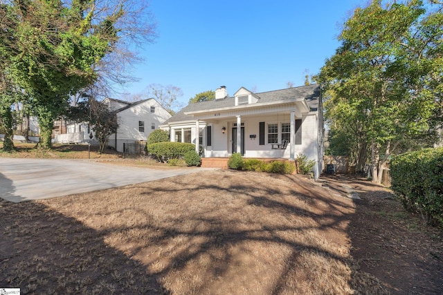 view of front facade with covered porch, a chimney, and fence