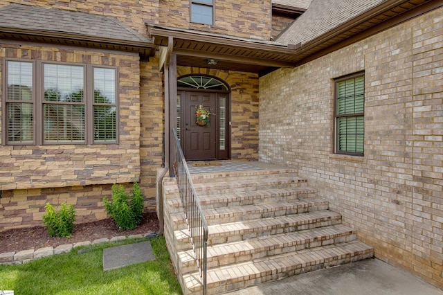 doorway to property featuring brick siding and roof with shingles