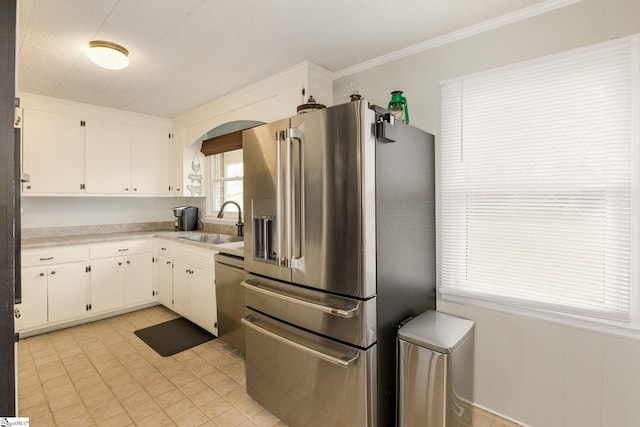 kitchen with ornamental molding, a sink, light countertops, appliances with stainless steel finishes, and white cabinetry