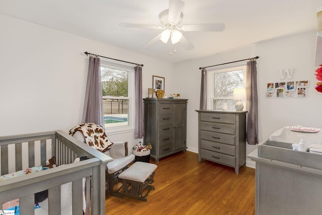 bedroom with a crib, wood finished floors, and a ceiling fan