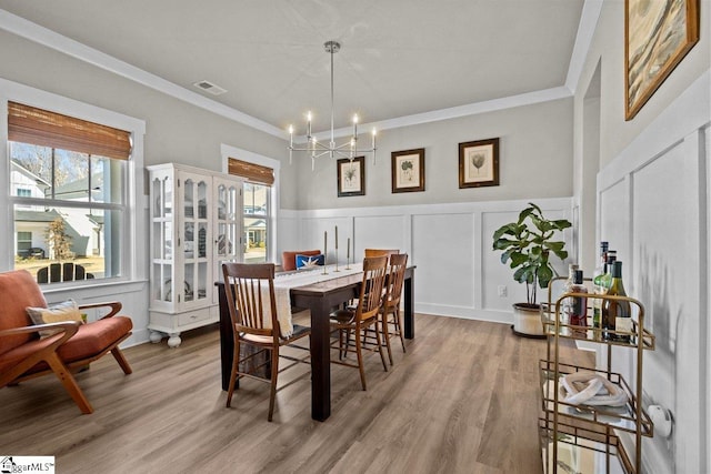 dining room featuring visible vents, ornamental molding, light wood-style floors, a decorative wall, and a chandelier