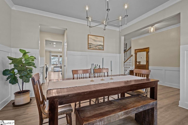 dining area with stairway, wood finished floors, a wainscoted wall, an inviting chandelier, and a decorative wall