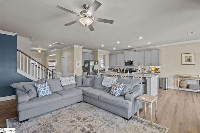 living room featuring stairway, light wood-style flooring, baseboards, and ornamental molding