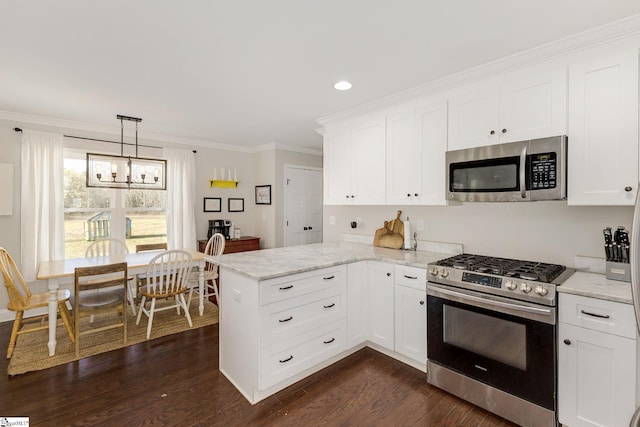 kitchen with a peninsula, dark wood-style flooring, ornamental molding, appliances with stainless steel finishes, and a chandelier