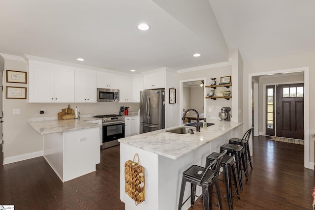 kitchen featuring a sink, stainless steel appliances, a peninsula, a breakfast bar area, and white cabinets