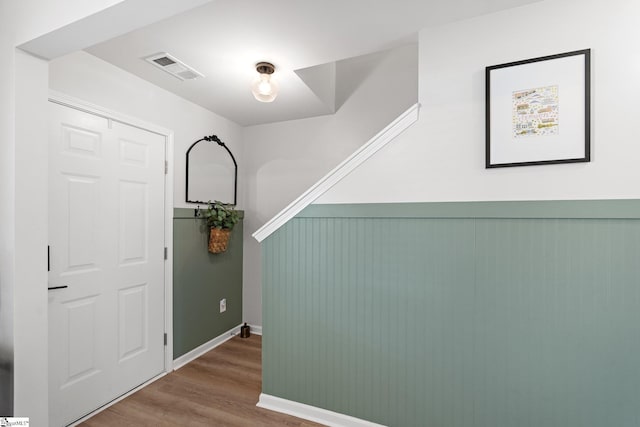 hall with wood finished floors, visible vents, and baseboards