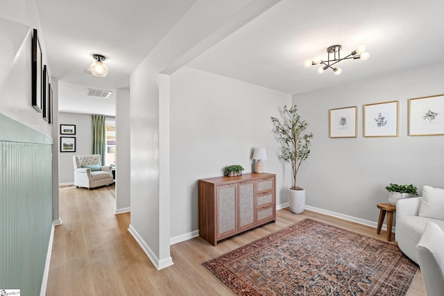 hallway with visible vents, baseboards, a chandelier, and light wood finished floors