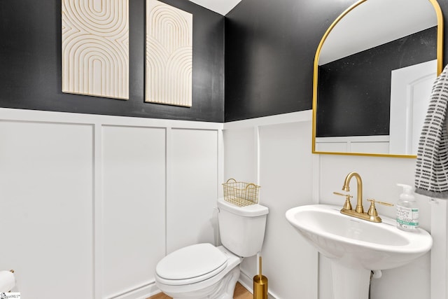 half bathroom with a decorative wall, wainscoting, toilet, and a sink