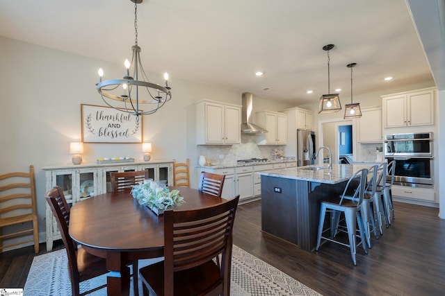 kitchen with a kitchen island with sink, appliances with stainless steel finishes, wall chimney range hood, a notable chandelier, and backsplash