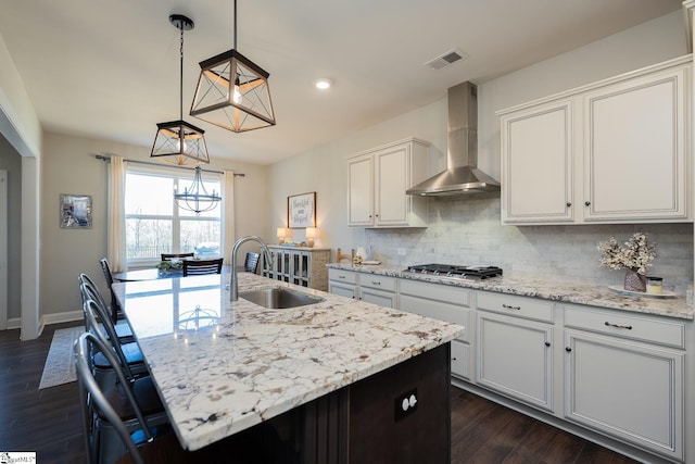 kitchen with visible vents, a sink, decorative backsplash, wall chimney exhaust hood, and a notable chandelier