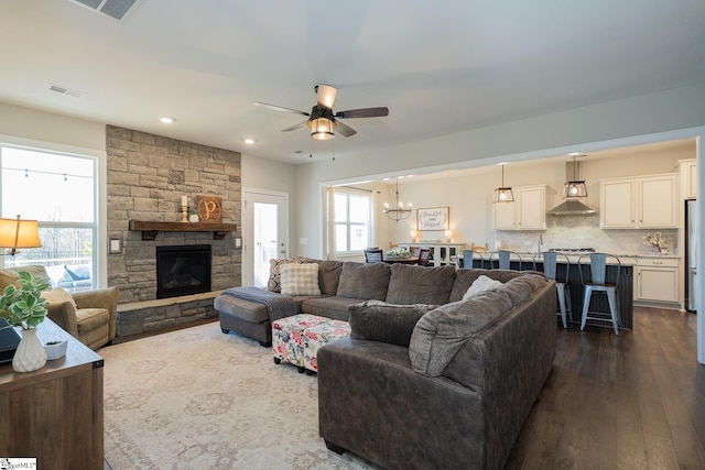 living room with visible vents, dark wood-style floors, a fireplace, and ceiling fan with notable chandelier