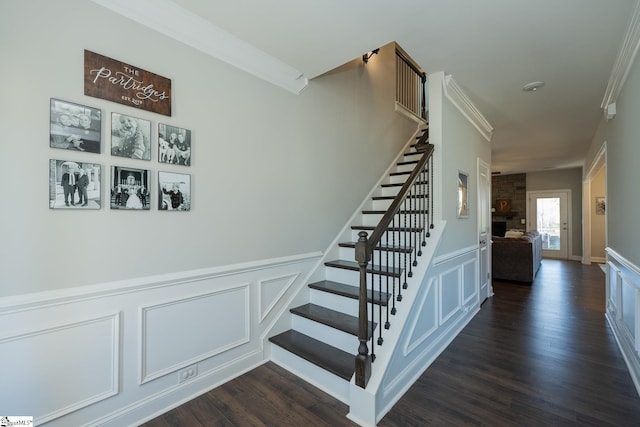 stairs featuring wood finished floors, ornamental molding, wainscoting, and a decorative wall