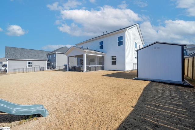 back of house featuring an outbuilding, a fenced backyard, a sunroom, a storage unit, and a lawn