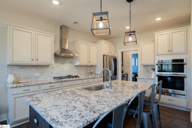 kitchen featuring visible vents, a sink, stainless steel appliances, wall chimney range hood, and decorative backsplash