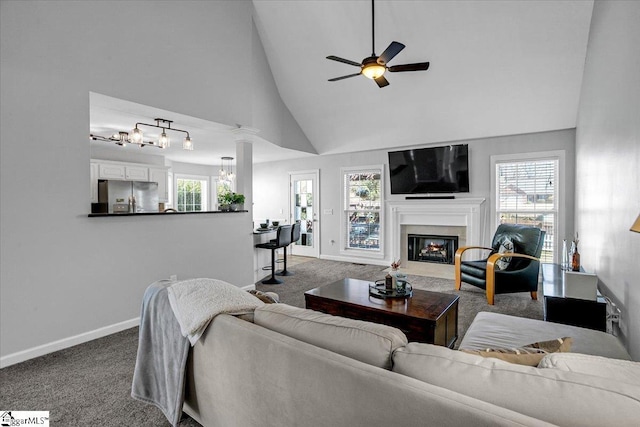 carpeted living room featuring a glass covered fireplace, ceiling fan with notable chandelier, high vaulted ceiling, and baseboards