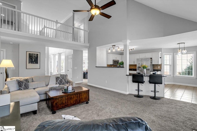 living area featuring a ceiling fan, decorative columns, light colored carpet, and baseboards