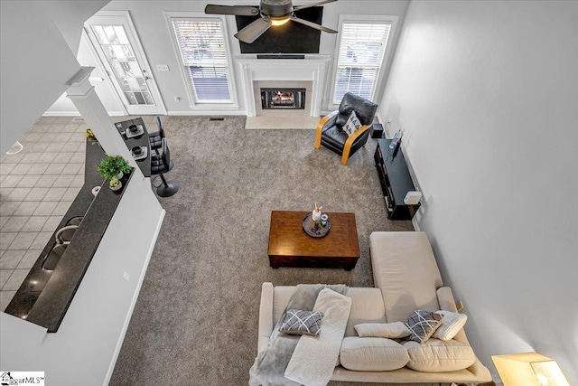 living area with a fireplace with flush hearth, a ceiling fan, and baseboards