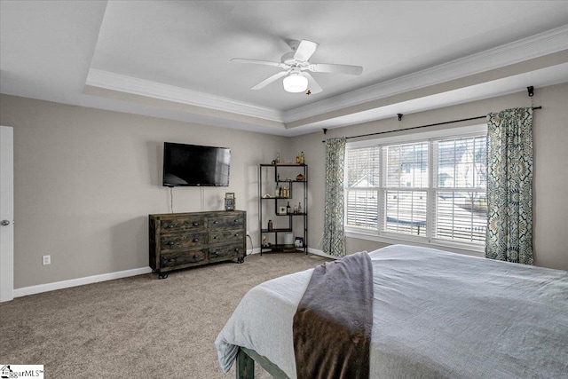 carpeted bedroom with a tray ceiling, a ceiling fan, baseboards, and ornamental molding