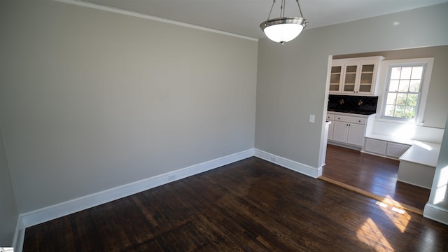 unfurnished dining area with crown molding, baseboards, and dark wood-style flooring