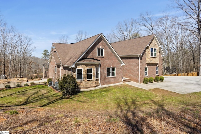 exterior space featuring brick siding, cooling unit, a yard, and roof with shingles