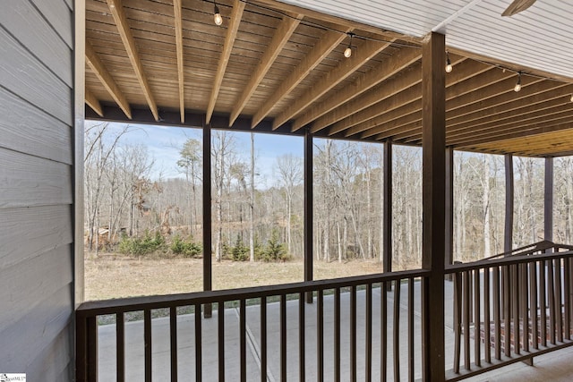 unfurnished sunroom featuring track lighting, a view of trees, and a wealth of natural light