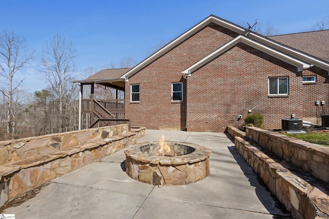 exterior space with central AC unit, stairs, a fire pit, a patio area, and brick siding