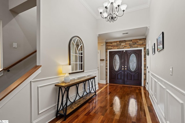 entryway featuring visible vents, a notable chandelier, ornamental molding, wood-type flooring, and wainscoting