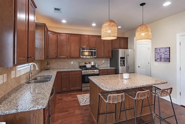 kitchen featuring dark wood-type flooring, a sink, backsplash, stainless steel appliances, and a breakfast bar area