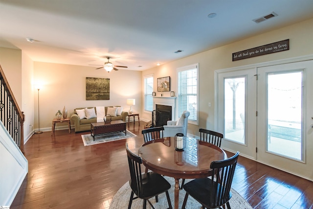 dining area featuring a ceiling fan, visible vents, a fireplace, dark wood-style flooring, and stairs