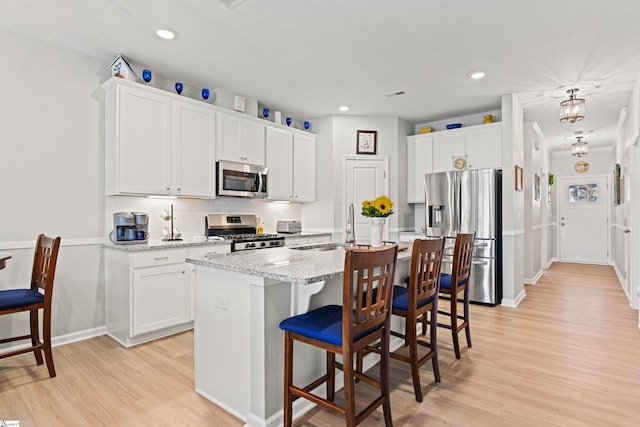 kitchen featuring a breakfast bar area, an island with sink, appliances with stainless steel finishes, light wood-type flooring, and backsplash