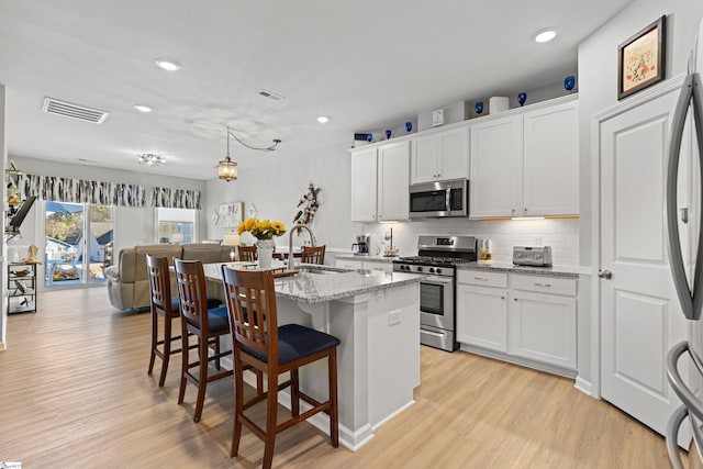 kitchen with a sink, a breakfast bar, light wood-type flooring, stainless steel appliances, and a kitchen island with sink