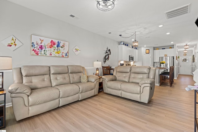 living room featuring light wood-type flooring, visible vents, and a chandelier