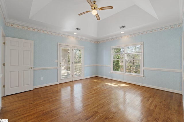 unfurnished room featuring visible vents, plenty of natural light, wood finished floors, wallpapered walls, and a raised ceiling