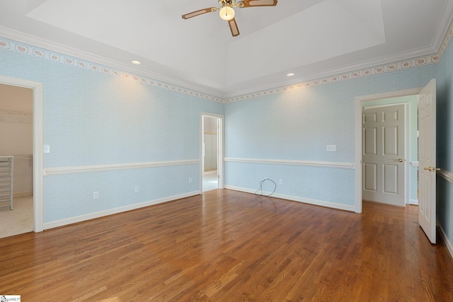 empty room with a raised ceiling, wood finished floors, crown molding, baseboards, and ceiling fan