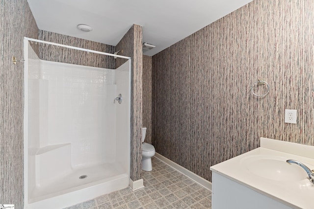 bathroom with vanity, toilet, a shower, and baseboards