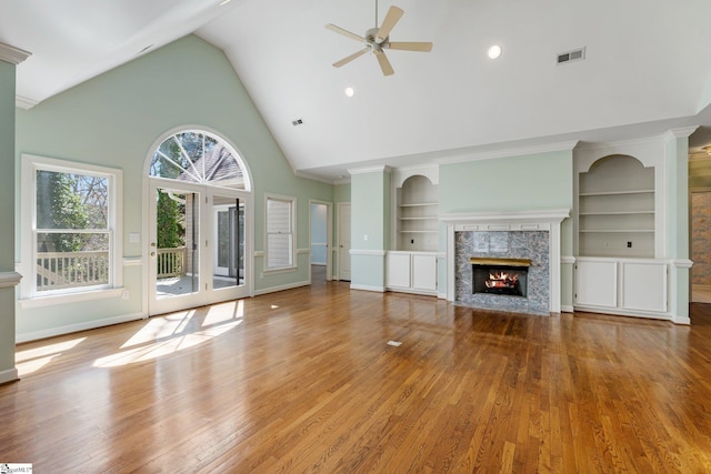 unfurnished living room with built in shelves, wood finished floors, a ceiling fan, visible vents, and a fireplace with flush hearth