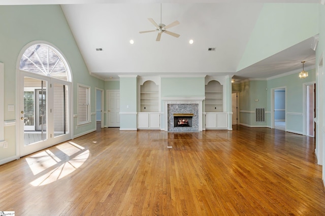 unfurnished living room with visible vents, built in shelves, a warm lit fireplace, and light wood-style flooring