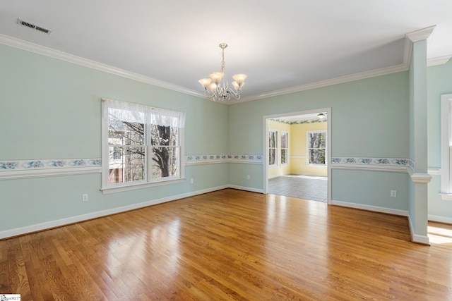 empty room featuring a chandelier, visible vents, ornamental molding, and wood finished floors