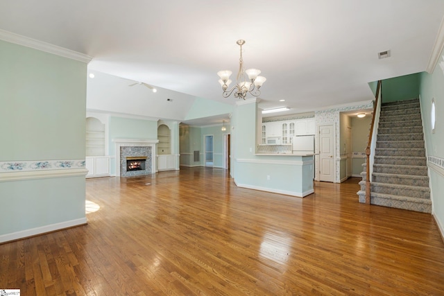 unfurnished living room with a notable chandelier, wood finished floors, stairway, a lit fireplace, and crown molding