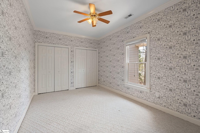 unfurnished bedroom with visible vents, wallpapered walls, ornamental molding, carpet flooring, and two closets