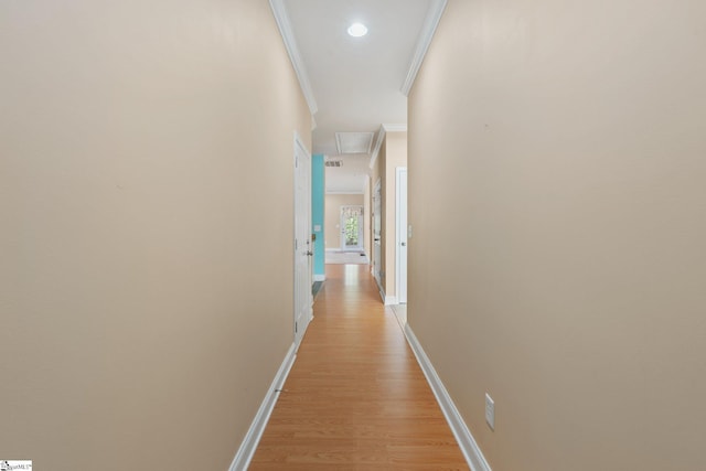 corridor featuring light wood finished floors, attic access, crown molding, and baseboards