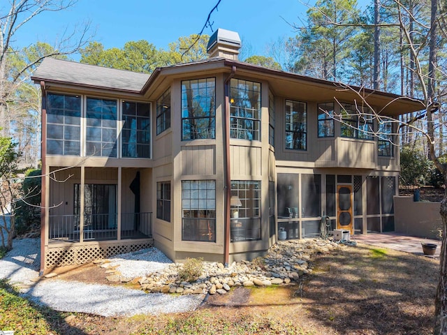 rear view of property featuring a chimney, a balcony, and a sunroom