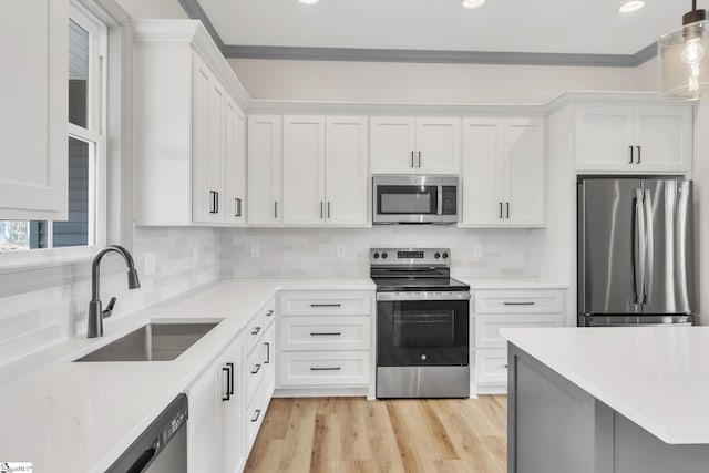 kitchen featuring light wood-type flooring, ornamental molding, stainless steel appliances, white cabinetry, and a sink