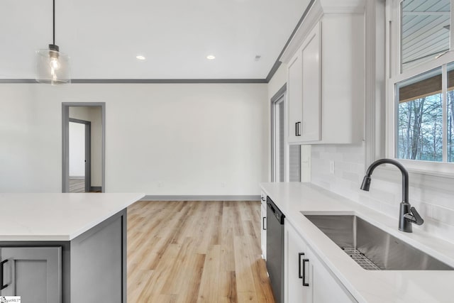 kitchen featuring tasteful backsplash, light wood finished floors, pendant lighting, light countertops, and a sink